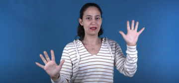  A woman is standing in front of a blue background, facing the camera with a neutral expression. She has her hands raised with palms facing outwards and fingers spread. She is wearing a white V-neck top with thin horizontal stripes.